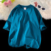 Türkisches, oversized Baumwoll-T-Shirt in Petrolblau auf weißem Plüsch neben Sonnenbrille und Teddybär.