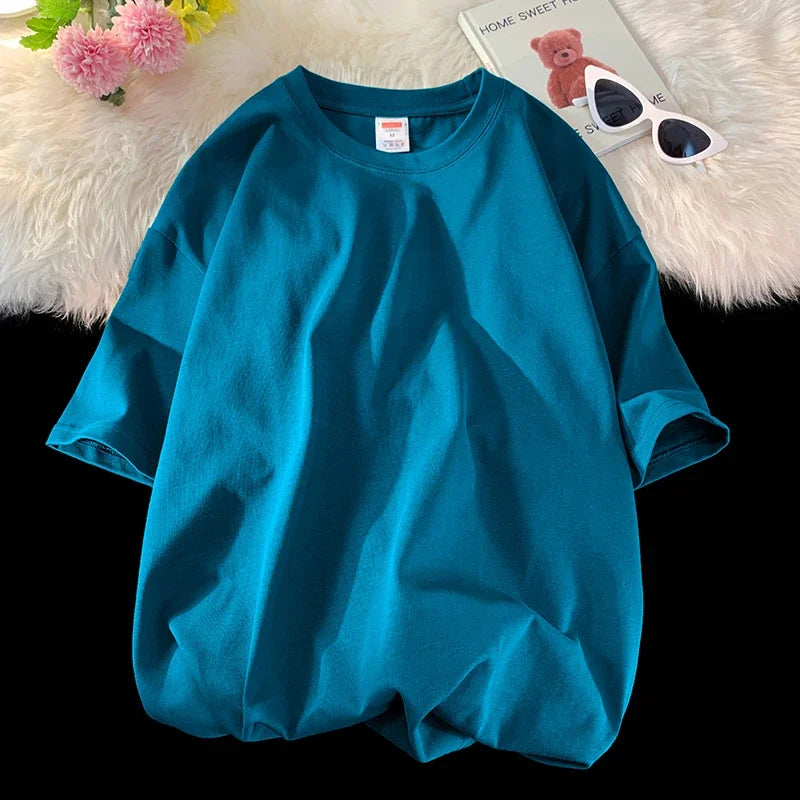 Türkisches, oversized Baumwoll-T-Shirt in Petrolblau auf weißem Plüsch neben Sonnenbrille und Teddybär.