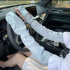 A person wearing white long-sleeved UV protection arm sleeves is shown inside a car, holding the steering wheel.