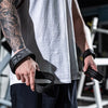 A person wearing a grey tank top is holding black gym wrist wraps for strength training.