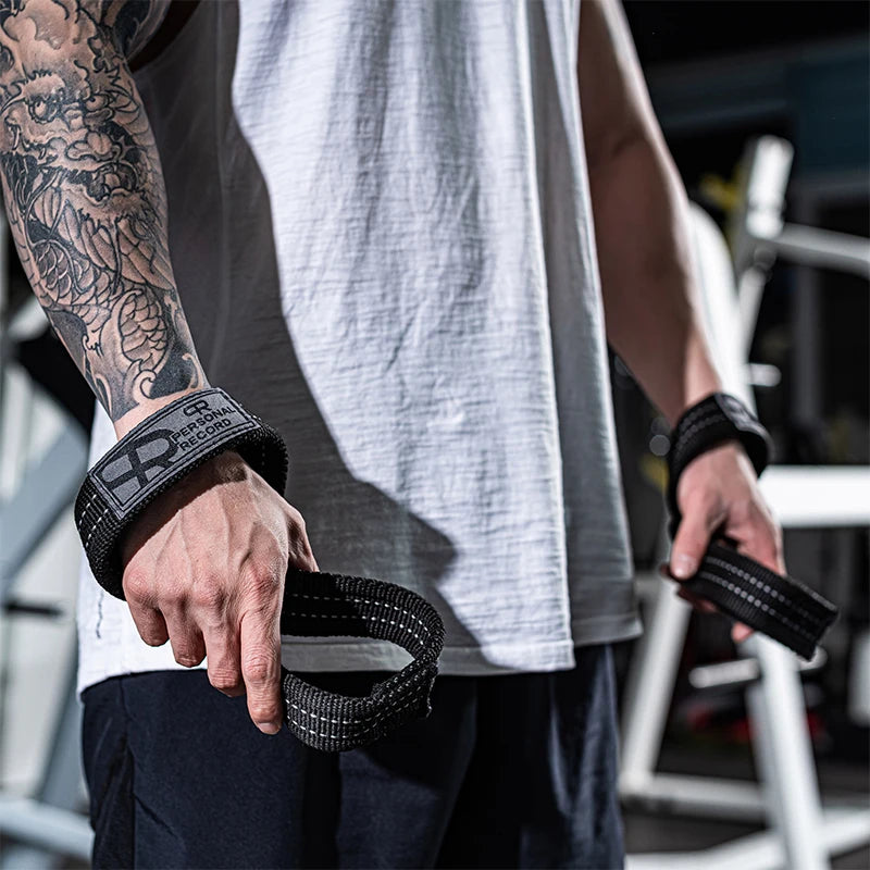 A person wearing a grey tank top is holding black gym wrist wraps for strength training.