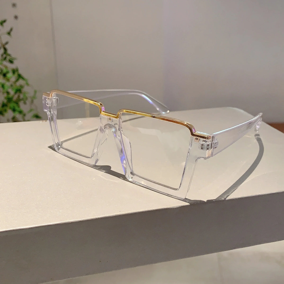 A pair of clear semi-rim metal eyeglasses with gold accents resting on a white surface.