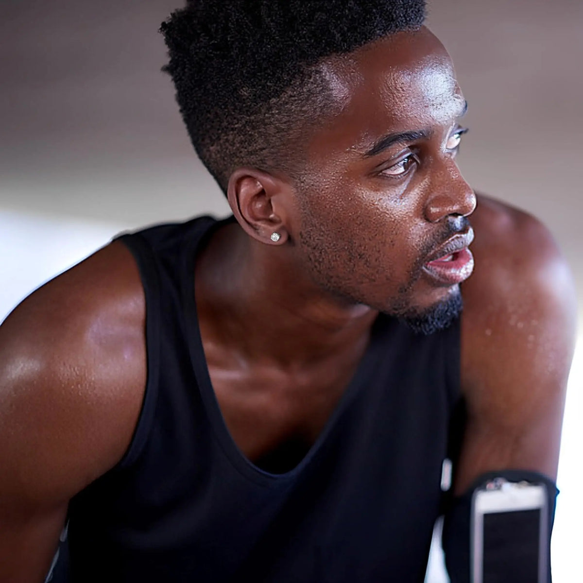 A man wearing a black tank top and stud earrings is shown in profile.