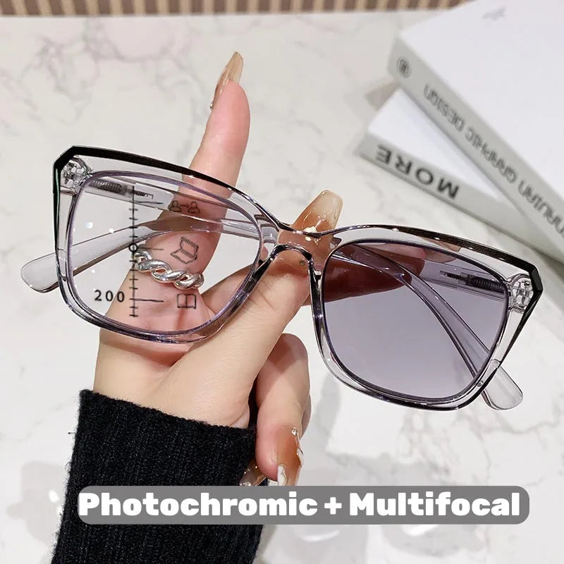 Eine Hand hält eine klare photochromische multifokale Brille mit grauen Linsen vor weißem Hintergrund.