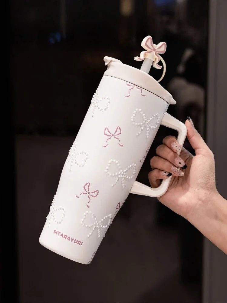 A hand holds a white insulated thermos mug decorated with pink pearl inlay patterns.
