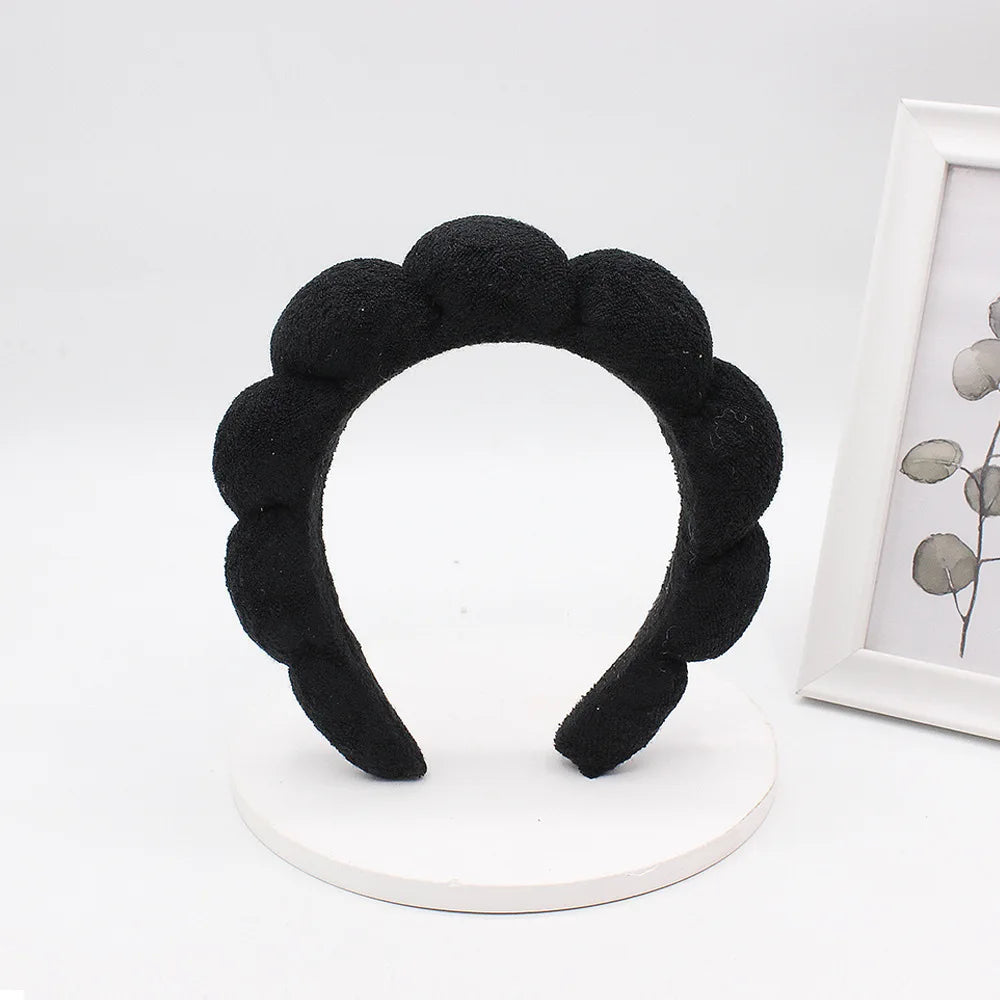 Black sponge terry cloth headband for hair styling displayed on a white circular stand.