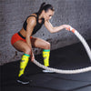 A woman wearing orange athletic shorts and yellow compression leg socks is performing a resistance exercise with a rope.