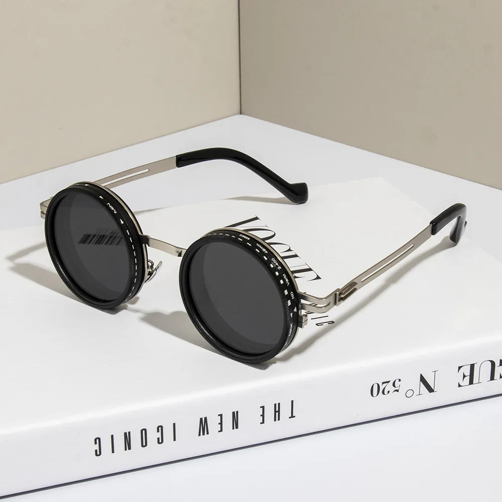 A pair of black round sunglasses with silver frames and adjustable dimming features resting on a white box.