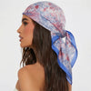 A woman models a blue and pink floral silk hair scarf tied around her hair.