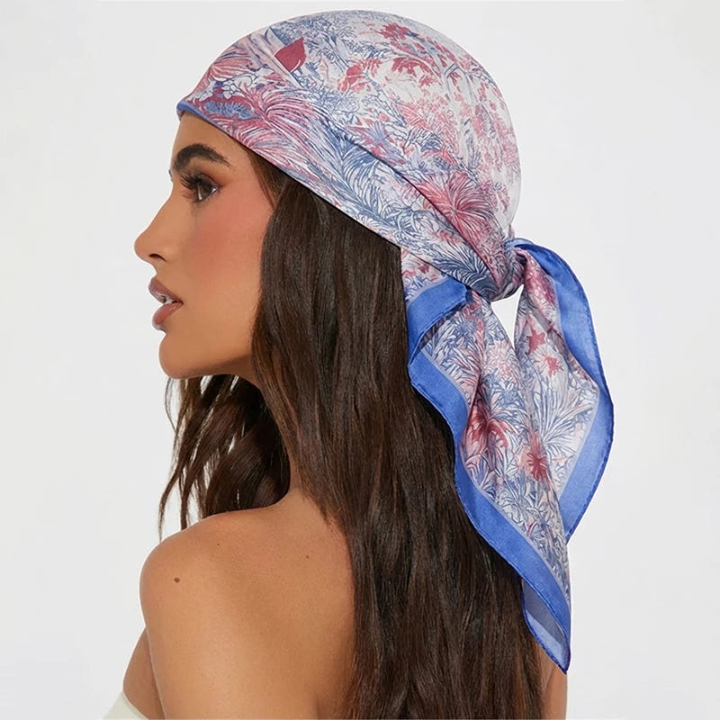 A woman models a blue and pink floral silk hair scarf tied around her hair.