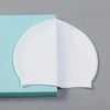 A white waterproof silicone swimming cap is shown resting on a light blue surface.