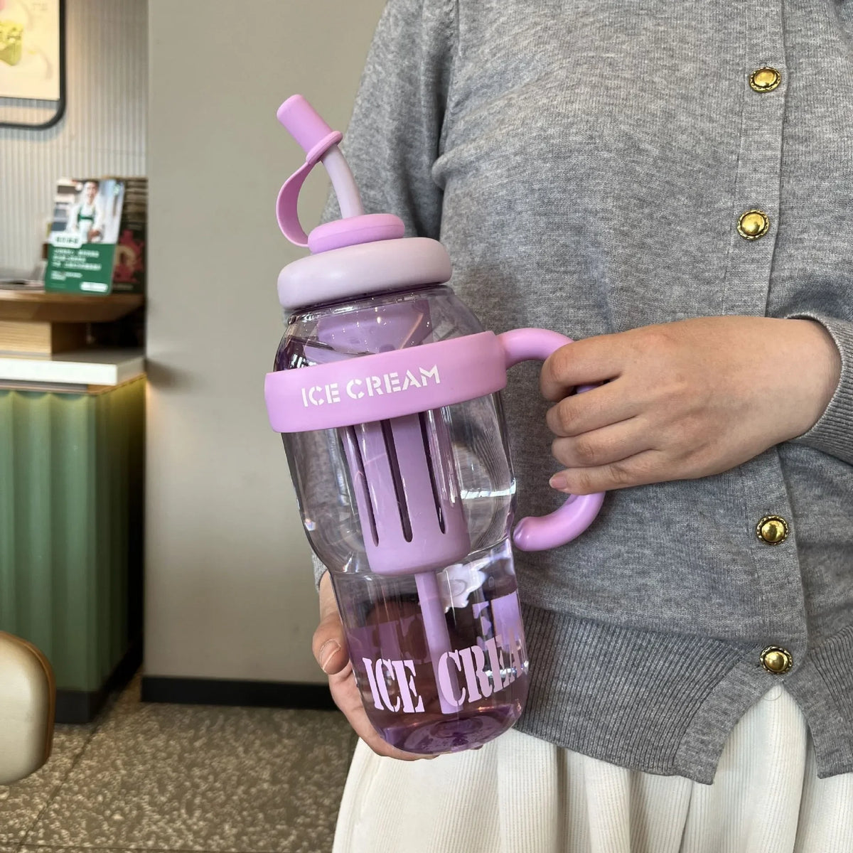 A person holds a purple plastic drinking cup labeled Ice Cream in a light gray cardigan.