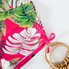 A vibrant pink and green floral print two-piece high-waist bikini set with a woven straw bag.