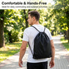 A man wearing a black nylon drawstring backpack walks down a paved path in a park.