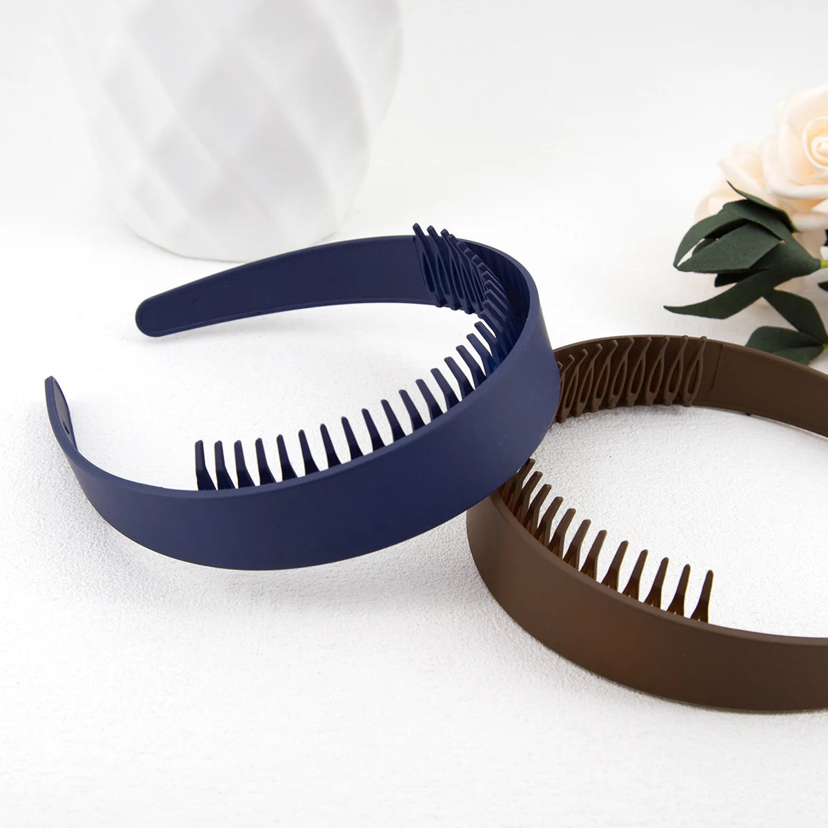 Dunkelblaue Plastik-Haarband mit Zähnen neben einem braunen Haarband auf weißem Untergrund.
