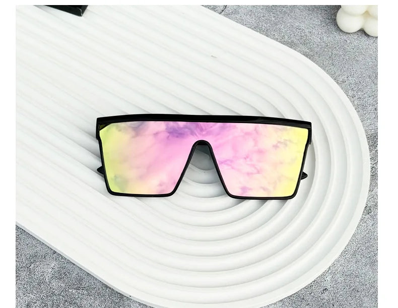 Retro square sunglasses with a vibrant pink and yellow gradient lens resting on a white, wavy surface.