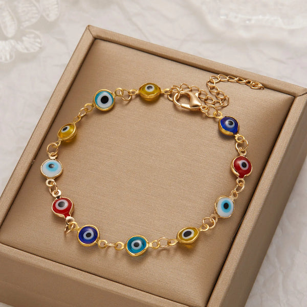 A gold charm bracelet featuring various colored evil eye charms presented in a light brown box.