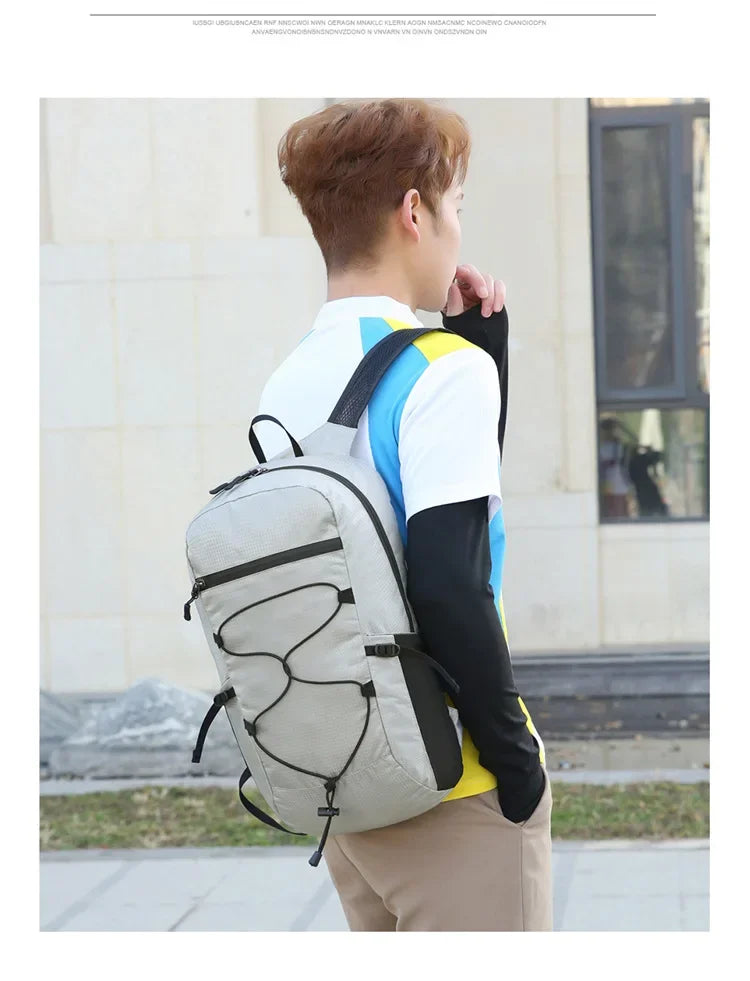 A person wearing a gray and blue backpack stands outdoors, looking to the side.
