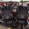 A pair of black leather motorcycle riding gloves featuring a pirate skull design on the back, displayed on a motorcycle.