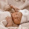 Neugeborenes Baby schläft friedlich in einem hellbeigen Baumwollturban und einer kuscheligen Strickdecke.
