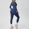 A woman wearing a navy blue performance yoga and gym set, including a long-sleeved top and leggings, standing in a neutral po