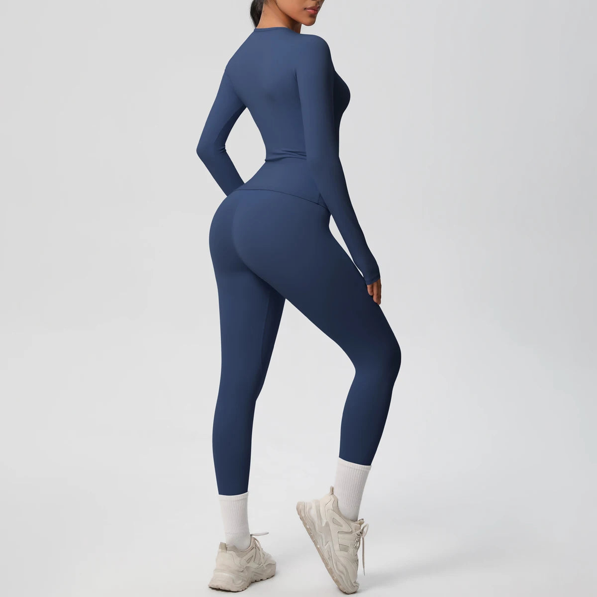 A woman wearing a navy blue performance yoga and gym set, including a long-sleeved top and leggings, standing in a neutral po