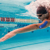 A swimmer performing a dive or stroke in a pool, splashing water and wearing a dark swim cap.