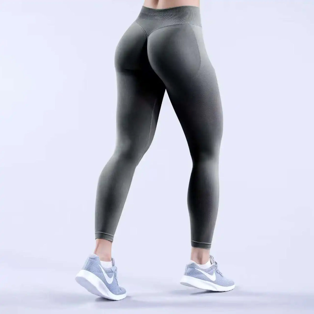 Eine Person trägt dunkelgraue, hochgeschnittene, nahtlose Yoga-Leggings und weiße Sportschuhe.