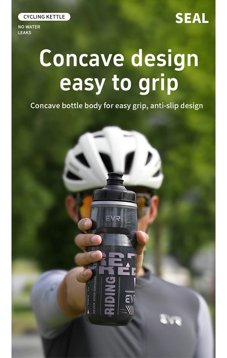 Una persona sostiene una botella de termo de ciclismo negra con agarre cóncavo, contra un fondo verde exterior desenfocado.