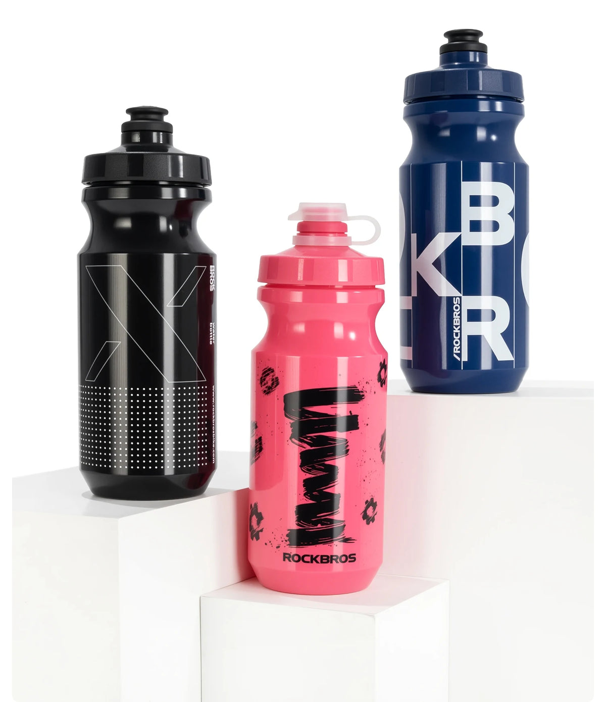 Un juego de tres botellas de agua para ciclismo resistentes en negro, rosa y azul sobre pedestales blancos.