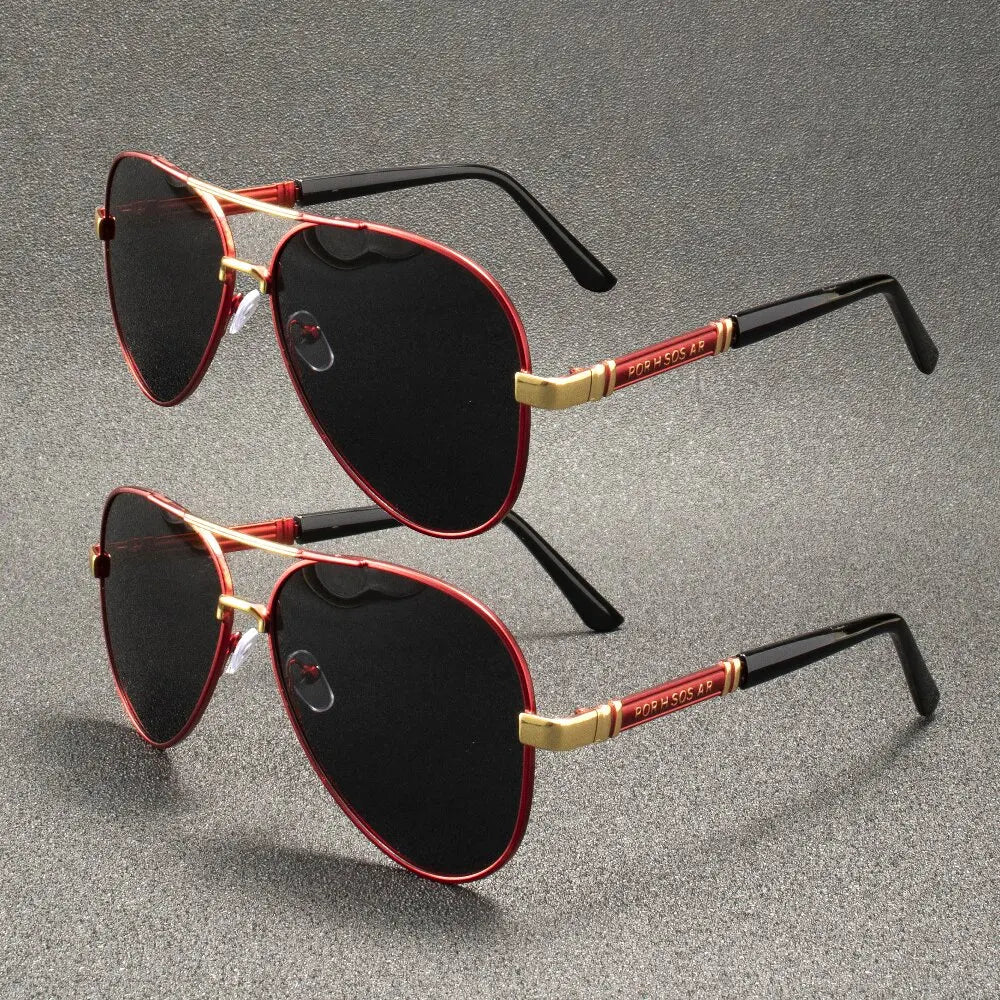 A pair of black sunglasses with red accents and gold detailing resting on a gray surface.