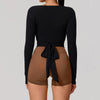 A woman wearing a black long sleeve top tied at the waist over a nude colored shorts.