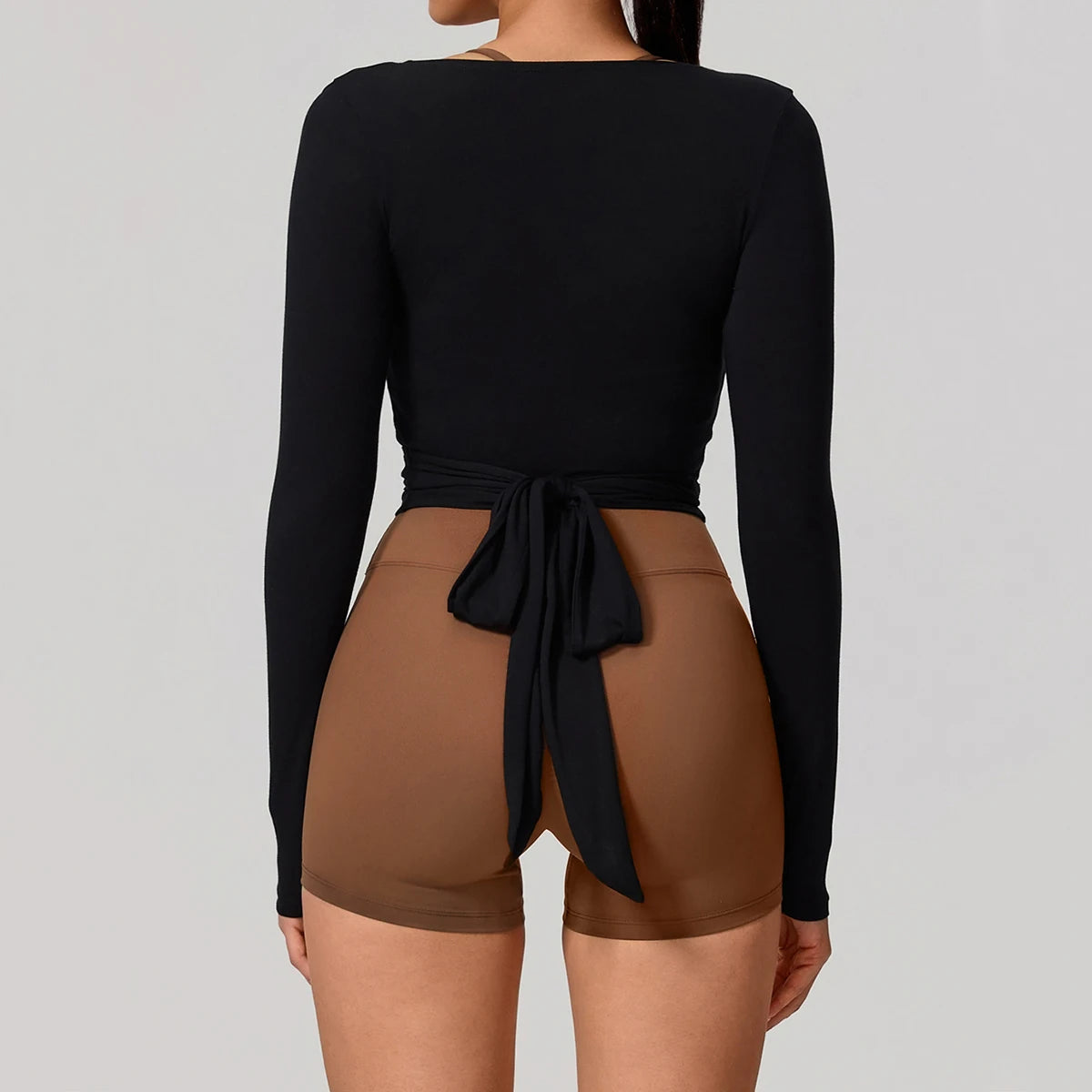 A woman wearing a black long sleeve top tied at the waist over a nude colored shorts.