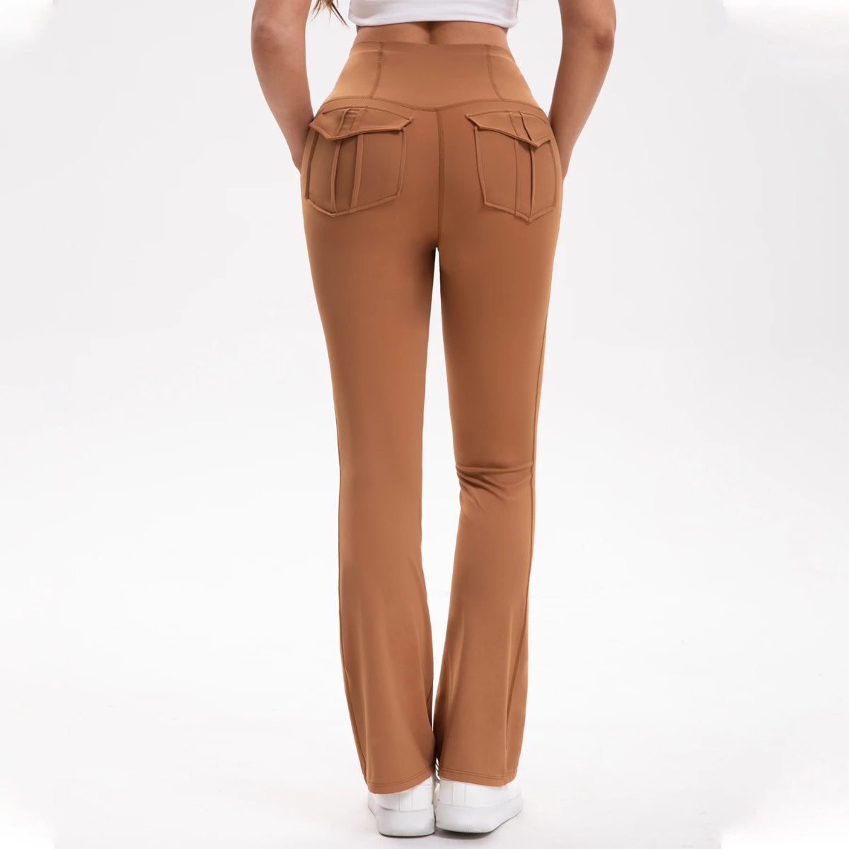 A model is wearing high-waisted brown yoga leggings with flap pockets and a white top.