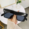 A hand holds a pair of black oversized square sunglasses against a white background.