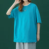 Eine Frau in einem leuchtend cyanfarbenen, oversized Baumwoll-T-Shirt mit einer silbernen Halskette und hellgrauen Hosen.
