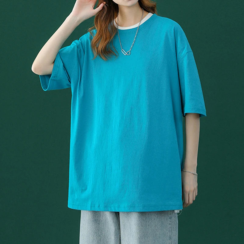 Eine Frau in einem leuchtend cyanfarbenen, oversized Baumwoll-T-Shirt mit einer silbernen Halskette und hellgrauen Hosen.