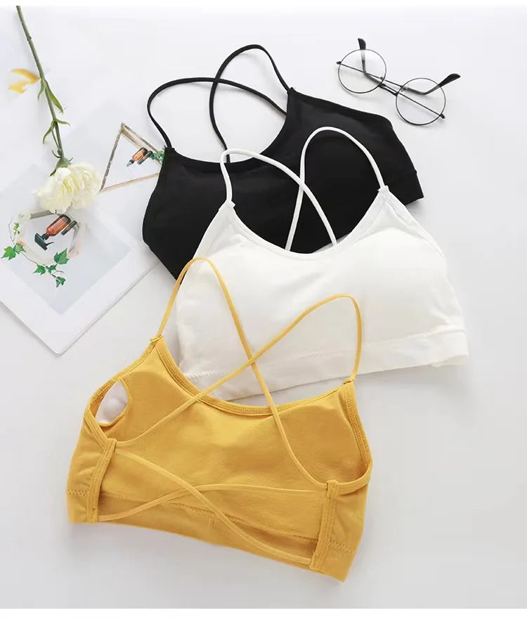 A collection of women's cross strap sports bras in black, white, and mustard yellow laid out on a white surface.