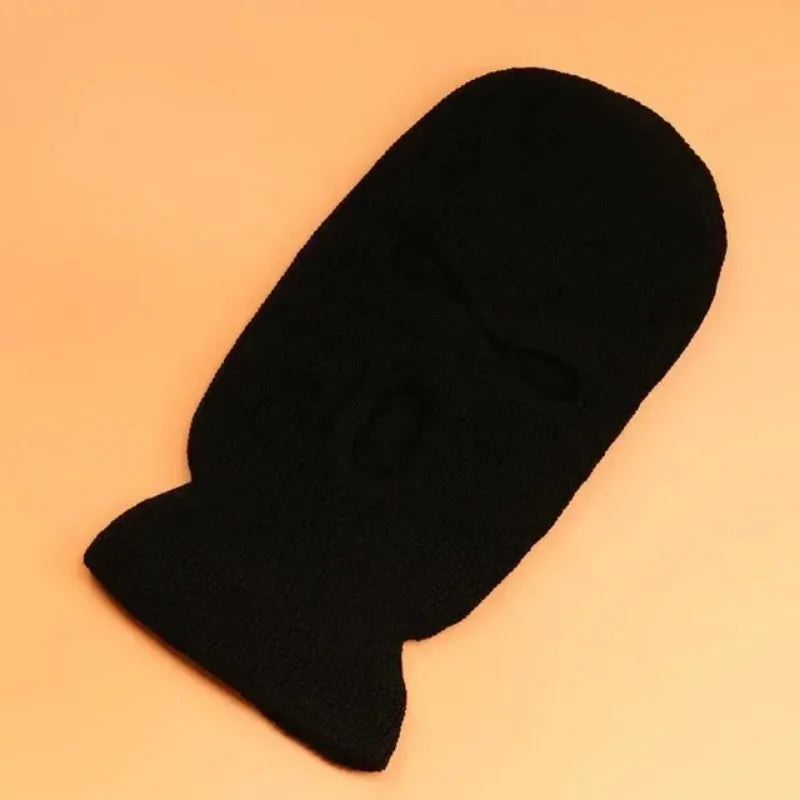 A black tactical knit balaclava beanie hat lying on a light orange background.