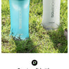 Una botella de agua deportiva de silicona transparente con tapa azul claro y texto blanco, mostrada al aire libre.