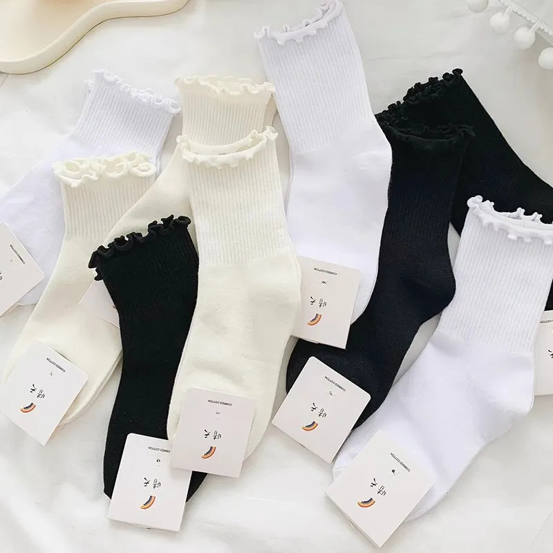 A stack of white and black cotton ruffle ankle socks displayed on a white surface.