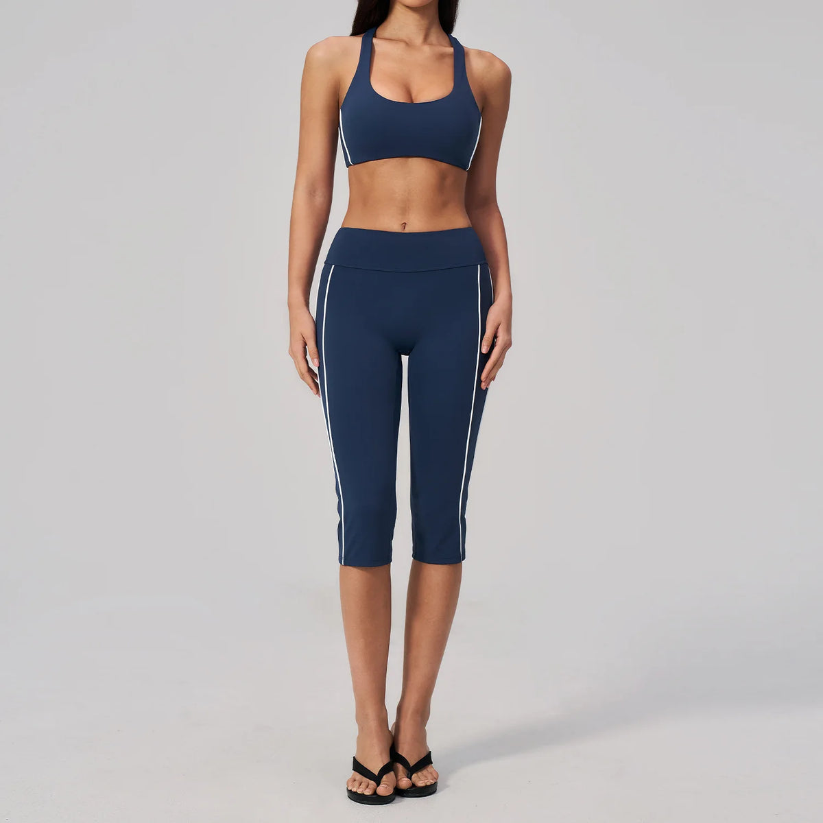 A woman wearing a navy blue two-piece yoga and sports tracksuit set consisting of a cropped top and full-length leggings.