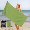 A woman holds up a large lime green microfiber quick-dry beach towel near the ocean.