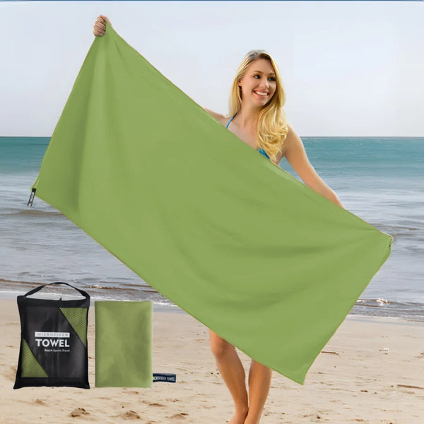 A woman holds up a large lime green microfiber quick-dry beach towel near the ocean.