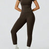 Model trägt ein dunkelbraunes Yoga-Set mit hohen Leggings und einem kurzärmeligen Oberteil.