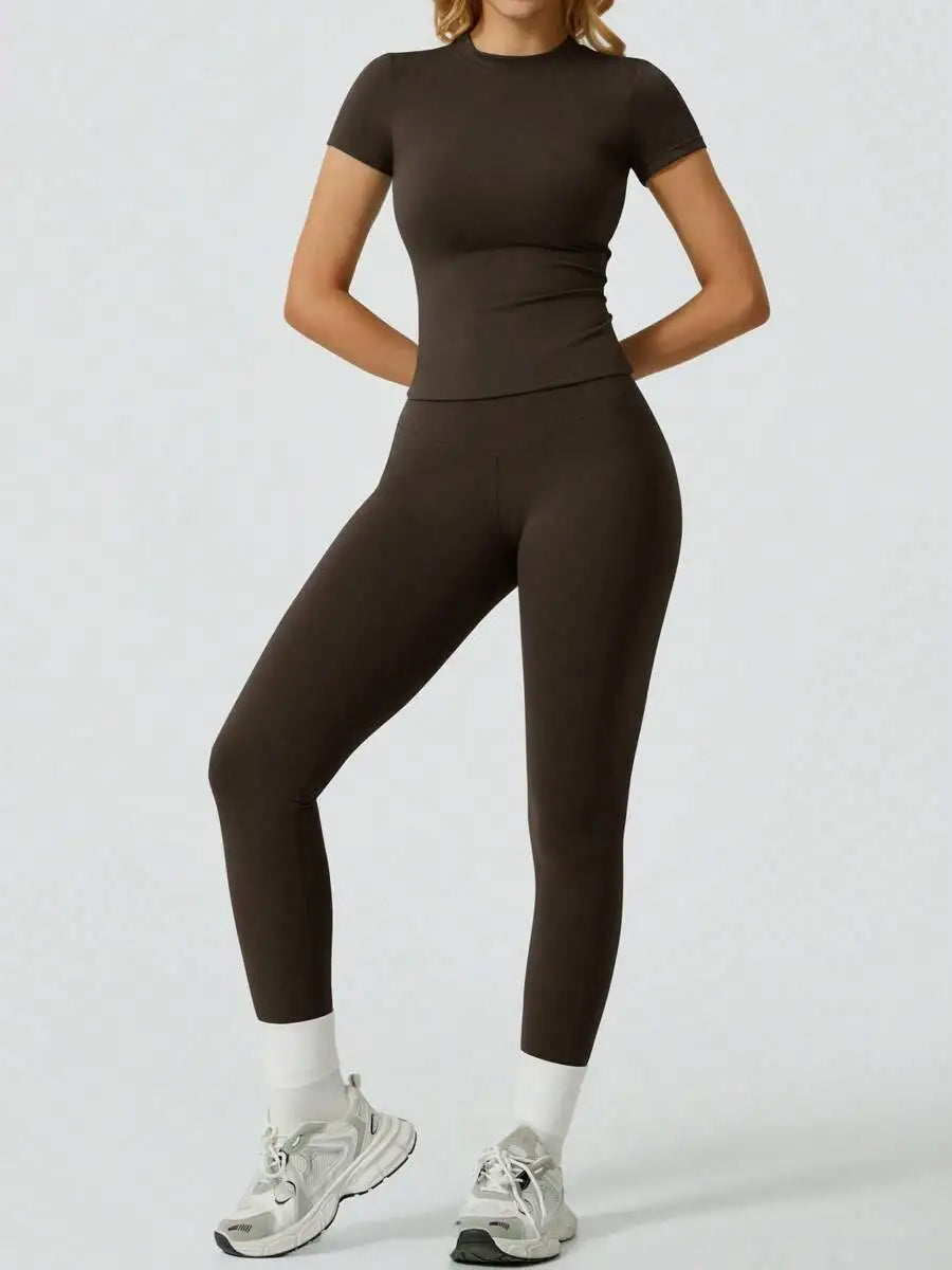 Model trägt ein dunkelbraunes Yoga-Set mit hohen Leggings und einem kurzärmeligen Oberteil.