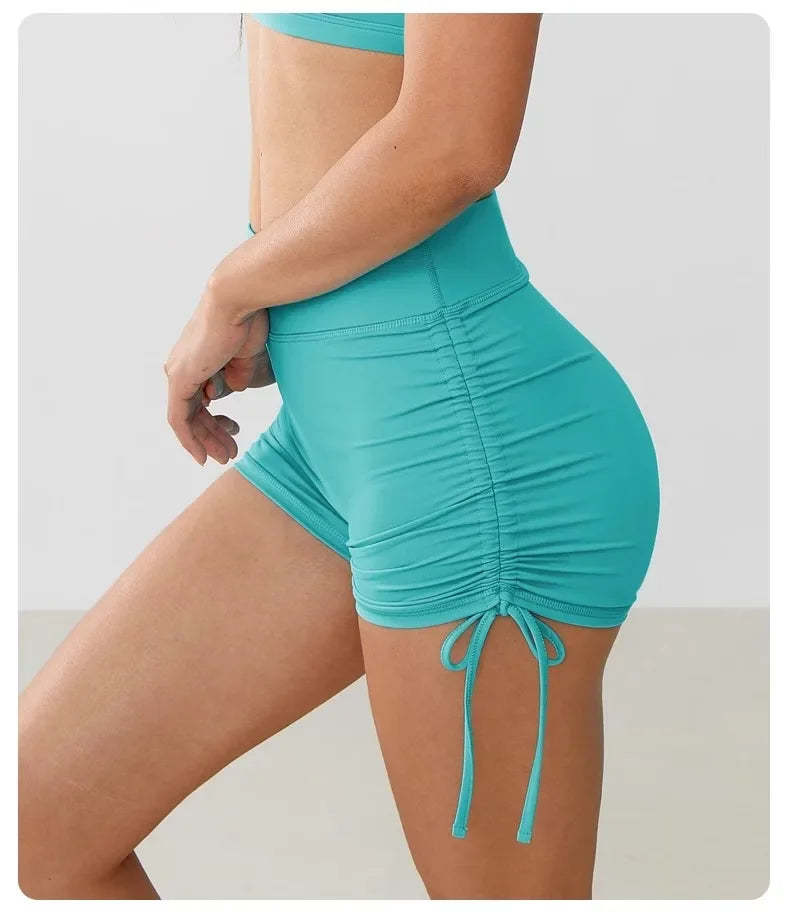 A model wears teal performance yoga shorts with a drawstring waist, highlighting the athletic fit.