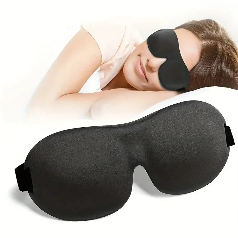 A black memory foam sleep mask is shown being worn by a person, with another mask lying nearby.