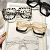 A display of four oversized rectangular reading glasses in various patterns and clear frames on a white tray.
