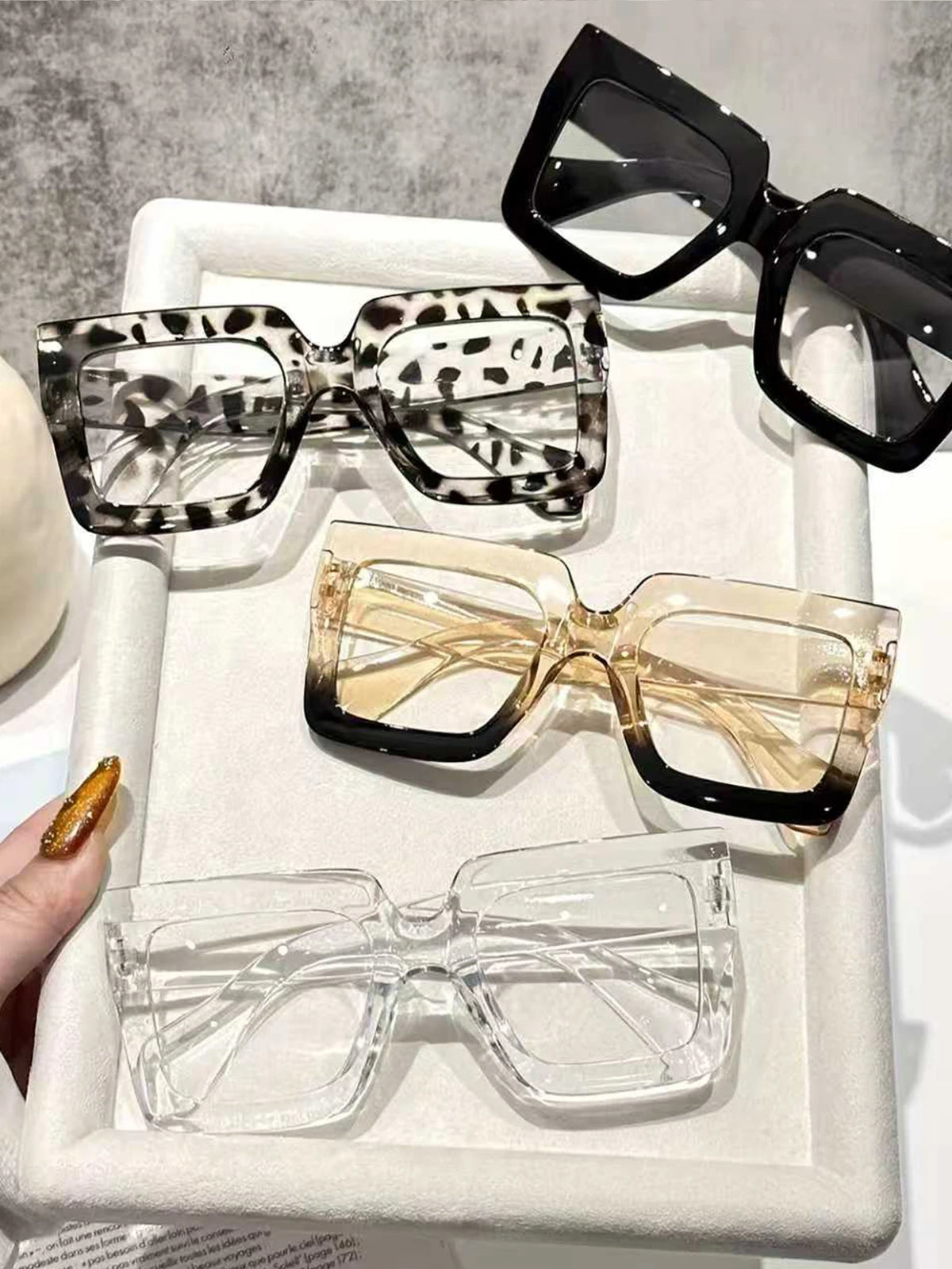 A display of four oversized rectangular reading glasses in various patterns and clear frames on a white tray.